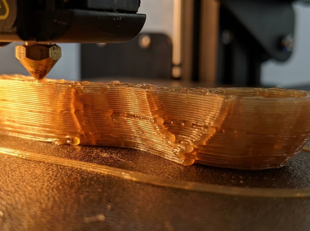Macro d'une pièce en PLA ambre, les cordons de matière déposés par la buse sont visibles.